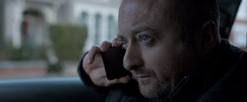 Movie still from “The Foreigner” (2017), directed by Martin Campbell – A man holding a cell phone up to his ear; Close Up shot, Low angle
