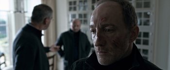 Movie still from “The Foreigner” (2017), directed by Martin Campbell – A man with a bunch of marks all over his face; Close Up shot, Over the shoulder angle