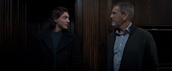 Movie still from “The Foreigner” (2017), directed by Martin Campbell – A man standing next to another man in front of a wooden wall; Medium shot, Over the shoulder angle