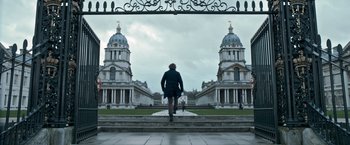 Movie still from “The Foreigner” (2017), directed by Martin Campbell – A man walking up steps in front of two large buildings; Extreme Wide shot, Low angle