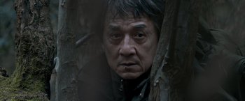 Movie still from “The Foreigner” (2017), directed by Martin Campbell – A person in a forest near a tree; Close Up shot, Low angle