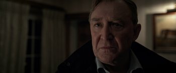 Movie still from “The Foreigner” (2017), directed by Martin Campbell – An older man in a black jacket looking at the camera; Close Up shot, Over the shoulder angle