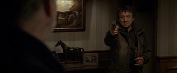 Movie still from “The Foreigner” (2017), directed by Martin Campbell – A man holding a gun in front of a horse; Medium shot, Over the shoulder angle
