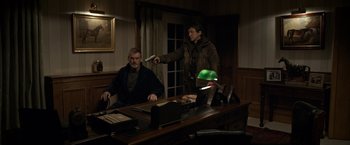 Movie still from “The Foreigner” (2017), directed by Martin Campbell – A man holding a remote in a room; Medium shot, Over the shoulder angle