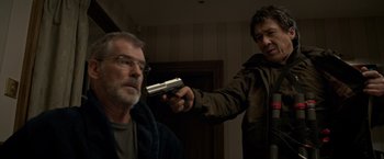 Movie still from “The Foreigner” (2017), directed by Martin Campbell – A man holding a gun pointed at another man; Medium shot, Over the shoulder angle