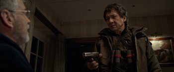 Movie still from “The Foreigner” (2017), directed by Martin Campbell – A man holding a gun in a room; Medium shot, Low angle