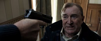 Movie still from “The Foreigner” (2017), directed by Martin Campbell – An older man is holding a gun up to his face; Close Up shot, Over the shoulder angle