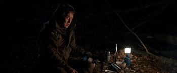 Movie still from “The Foreigner” (2017), directed by Martin Campbell – A man sitting in the dark near a campfire; Medium shot, High angle