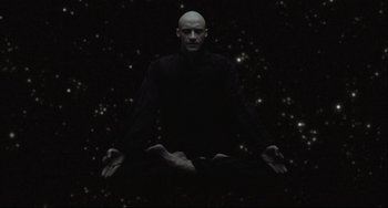 Movie still from “The Fountain” (2006), directed by Darren Aronofsky – A bald man sitting on the ground in front of a star filled sky; Medium shot, Overhead angle