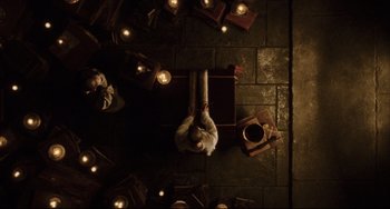 Movie still from “The Fountain” (2006), directed by Darren Aronofsky – An overhead view of a person sitting in a chair with candles; Extreme Wide shot, Overhead angle