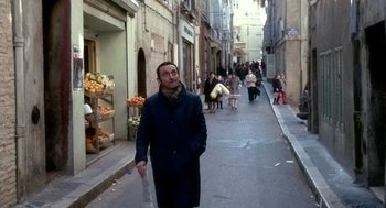 Movie still from “The French Connection” (1971), directed by William Friedkin – A man walking down a street holding a newspaper; Medium shot, Over the shoulder angle