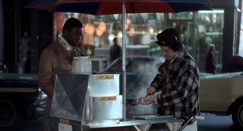 Movie still from “The French Connection” (1971), directed by William Friedkin – Two men standing next to each other at an outdoor food stand; Medium shot, High angle