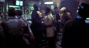 Movie still from “The French Connection” (1971), directed by William Friedkin – A group of people standing around a bar; Wide shot, High angle