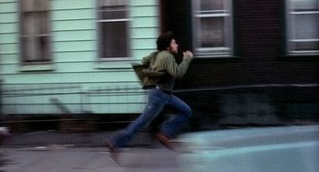 Movie still from “The French Connection” (1971), directed by William Friedkin – A man running down the street with a backpack on; Wide shot, High angle