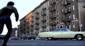 Movie still from “The French Connection” (1971), directed by William Friedkin – A couple of cars parked in front of a tall building; Extreme Wide shot, Low angle