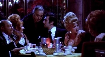 Movie still from “The French Connection” (1971), directed by William Friedkin – A group of people sitting at a table with food; Medium shot, Over the shoulder angle
