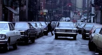 Movie still from “The French Connection” (1971), directed by William Friedkin – A man walking down a street next to parked cars; Wide shot, Low angle