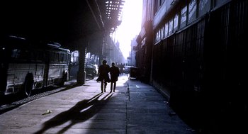 Movie still from “The French Connection” (1971), directed by William Friedkin – Two people walking down a sidewalk near a building; Wide shot, Low angle