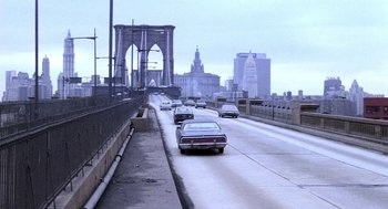 Movie still from “The French Connection” (1971), directed by William Friedkin – Cars driving down a road on a cloudy day; Extreme Wide shot, High angle