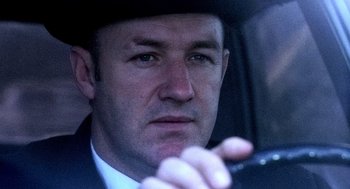 Movie still from “The French Connection” (1971), directed by William Friedkin – A person in a car wearing a hat; Close Up shot, Low angle