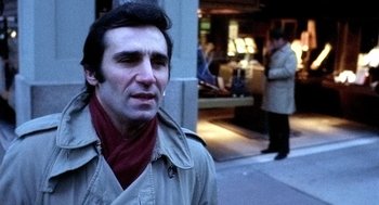 Movie still from “The French Connection” (1971), directed by William Friedkin – A man wearing a trench coat and a red scarf; Close Up shot, Over the shoulder angle