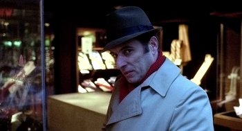 Movie still from “The French Connection” (1971), directed by William Friedkin – A man wearing a hat and a trench coat; Close Up shot, Over the shoulder angle