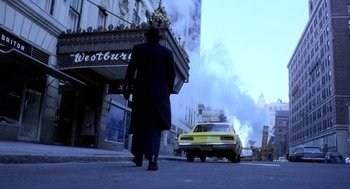 Movie still from “The French Connection” (1971), directed by William Friedkin – A man walking down the street in front of a building with smoke billowing out of it; Wide shot, Low angle