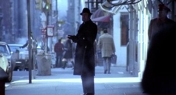 Movie still from “The French Connection” (1971), directed by William Friedkin – A man standing on the sidewalk holding a cell phone; Wide shot, Low angle