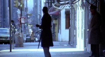 Movie still from “The French Connection” (1971), directed by William Friedkin – A man walking down the street holding a cell phone; Wide shot, Low angle