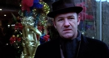 Movie still from “The French Connection” (1971), directed by William Friedkin – A man wearing a hat and a black jacket; Close Up shot, Low angle