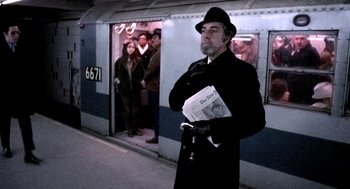 Movie still from “The French Connection” (1971), directed by William Friedkin – A man standing in front of a train holding a newspaper; Medium shot, Over the shoulder angle