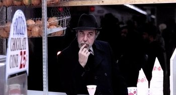 Movie still from “The French Connection” (1971), directed by William Friedkin – A man in a black coat and a black hat smoking a cigarette; Close Up shot, Low angle