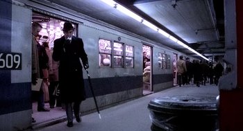 Movie still from “The French Connection” (1971), directed by William Friedkin – A man in a suit and hat walking down a train platform; Wide shot, Low angle