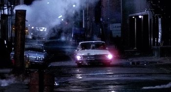 Movie still from “The French Connection” (1971), directed by William Friedkin – A car driving down a street at night with smoke billowing from the headlights; Wide shot, Low angle