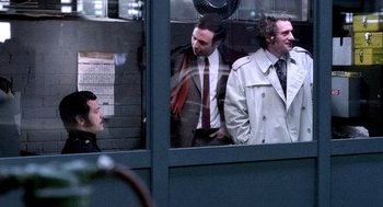 Movie still from “The French Connection” (1971), directed by William Friedkin – A group of men standing next to each other in front of a window; Medium shot, Over the shoulder angle