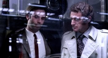 Two men in suits and ties looking at each other through a window