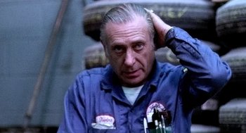 Movie still from “The French Connection” (1971), directed by William Friedkin – An older man in a blue work shirt is holding his hand up to his head; Close Up shot, Low angle