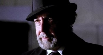 Movie still from “The French Connection” (1971), directed by William Friedkin – A man with a beard wearing a suit and a hat; Close Up shot, Low angle