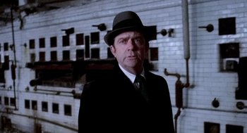 Movie still from “The French Connection” (1971), directed by William Friedkin – A man wearing a suit and a hat standing in front of a building; Close Up shot, Low angle
