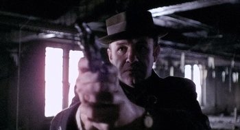 Movie still from “The French Connection” (1971), directed by William Friedkin – A man wearing a hat and holding a gun in his hand; Close Up shot, Low angle