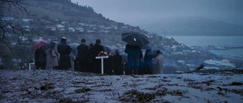 Movie still from “The Frighteners” (1996), directed by Peter Jackson – A group of people sitting under umbrellas in the snow; Extreme Wide shot, High angle