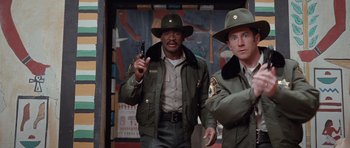 Movie still from “The Frighteners” (1996), directed by Peter Jackson – A couple of men standing next to each other holding a gun; Medium shot, Low angle