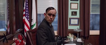 Movie still from “The Frighteners” (1996), directed by Peter Jackson – A man in a suit and tie sitting at a desk in a room; Close Up shot, Over the shoulder angle