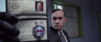 Movie still from “The Frighteners” (1996), directed by Peter Jackson – A man in a suit and tie in front of a police badge; Close Up shot, Low angle