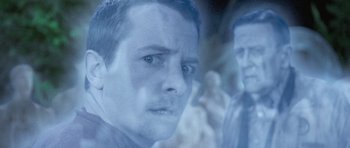 Movie still from “The Frighteners” (1996), directed by Peter Jackson – A man is looking at the camera with a blurry image behind him; Close Up shot, Over the shoulder angle