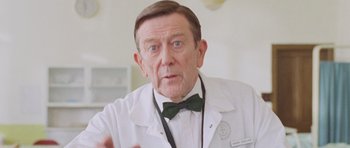 Movie still from “The Frighteners” (1996), directed by Peter Jackson – An older man wearing a white lab coat and a green bow tie; Close Up shot, Low angle