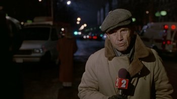 Movie still from “The Fugitive” (1993), directed by Andrew Davis – A man is standing on the sidewalk while holding a microphone; Close Up shot, Over the shoulder angle