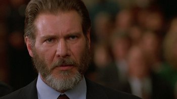 Movie still from “The Fugitive” (1993), directed by Andrew Davis – A man with a beard and a suit and tie in front of a group of people; Close Up shot, Low angle