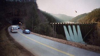 Movie still from “The Fugitive” (1993), directed by Andrew Davis – A car driving down a road next to a bridge; Extreme Wide shot, High angle