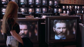 Movie still from “The Fugitive” (1993), directed by Andrew Davis – A bunch of tvs with a man's face on them; Medium shot, Over the shoulder angle